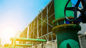 Industrial cooling tower system with large green water pipes and valve in foreground, illustrating sustainable water treatment and facility operations.